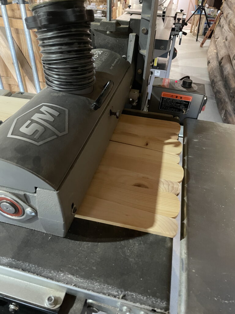 Wooden panels undergoing precision sanding with an industrial drum sander in a woodworking studio. The image highlights professional craftsmanship, modern machinery, and sustainable material preparation for bespoke furniture design projects.