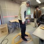 Instructor testing the strength of a CNC-machined panel by stepping on it in a fabrication workshop