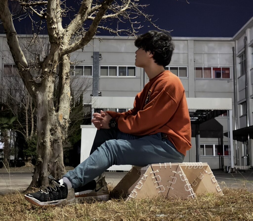 Student sitting on a digitally fabricated stool made from parametric design elements, displayed in an outdoor setting near a tree.