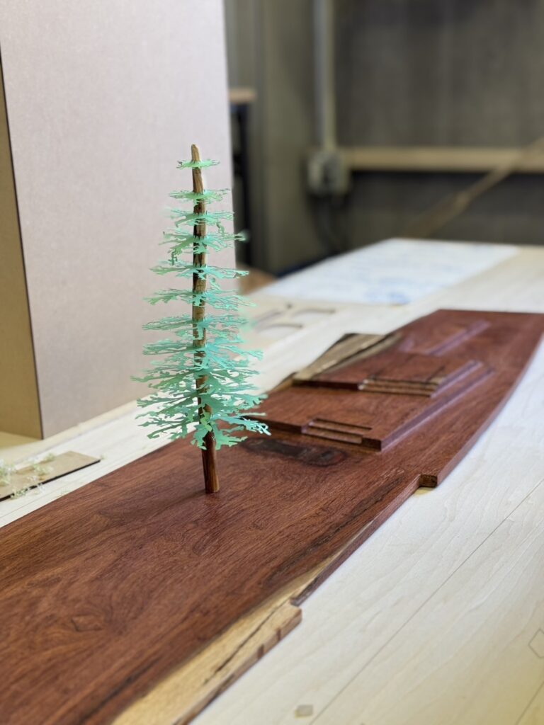 Architectural model with a CNC-machined wood base and a 3D-printed tree, illustrating site-specific design and fabrication techniques